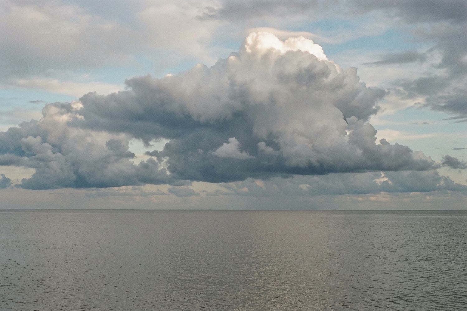 A bank of cumulus building over open water, the top edge lit and the sea pewter.