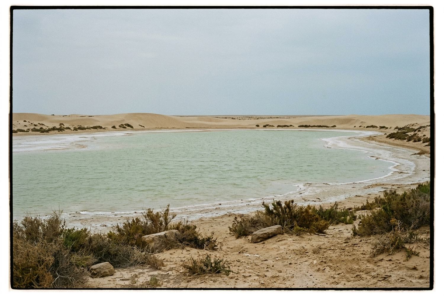 A shallow desert lagoon of pale green water rimmed by low dunes and salt flats.