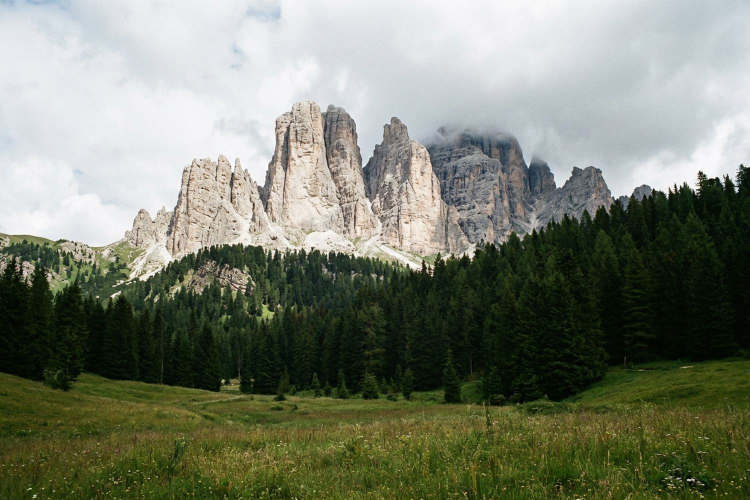 Pale limestone towers above dark pine forest with cloud building at the summits.
