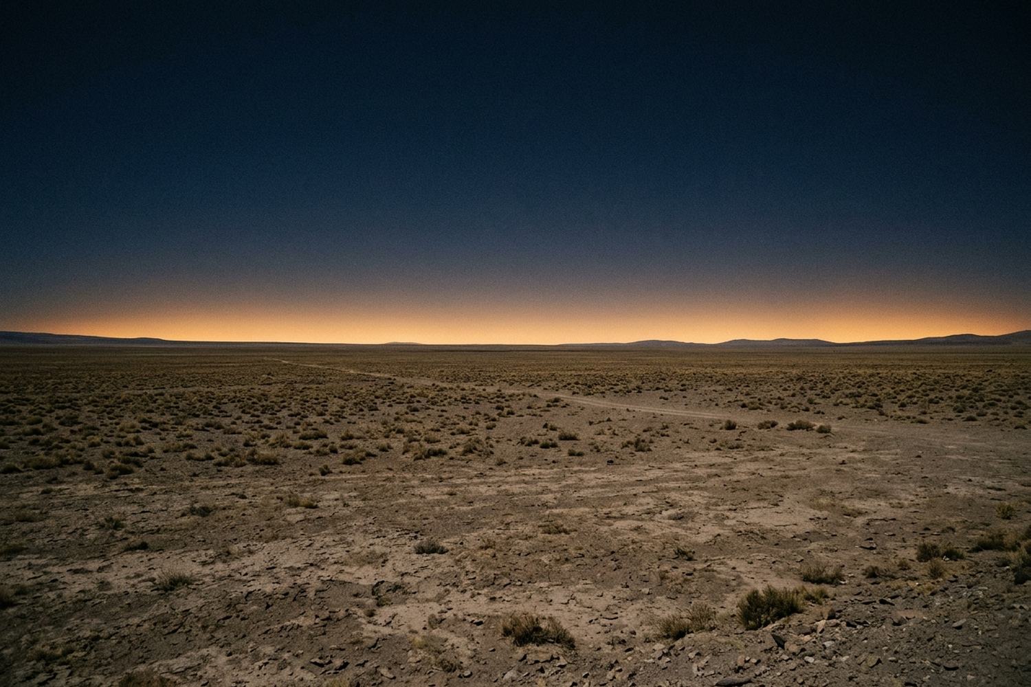 A high desert plain under a deep indigo daytime sky with the horizon glowing orange.
