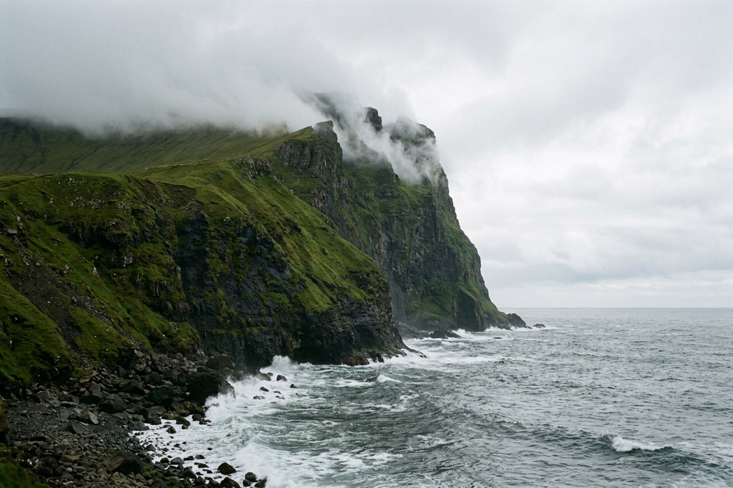 A vertical green sea cliff dropping into gray Atlantic water with cloud tearing over.