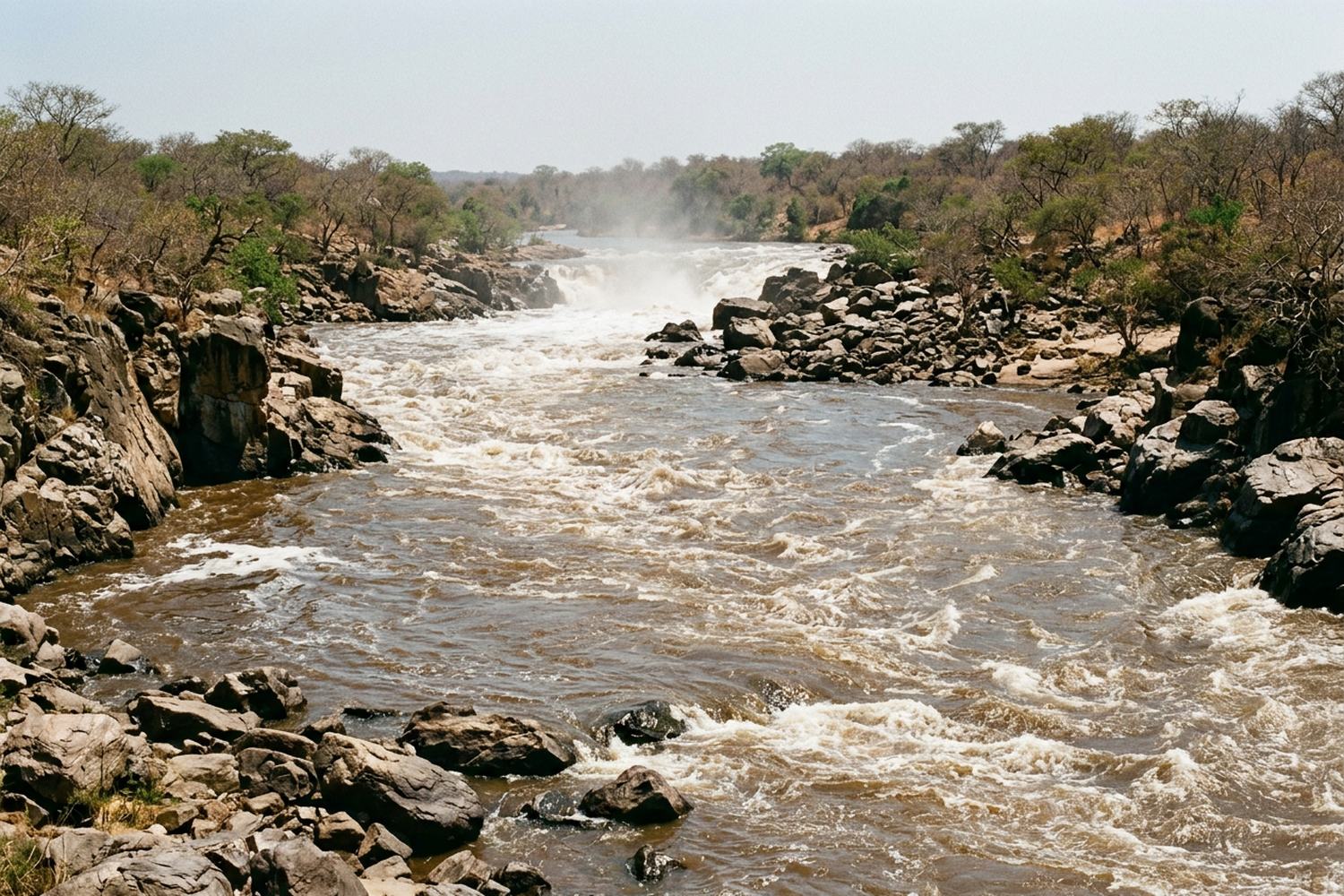 A broad brown river running fast between rocky banks, spray haze in the distance.